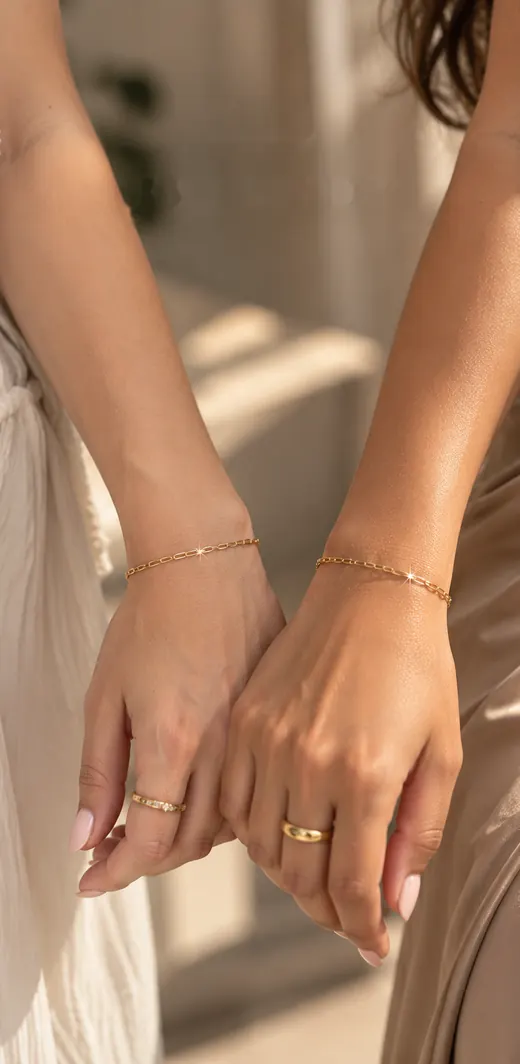 Two friends holding hands, each wearing a matching fine gold bracelet
