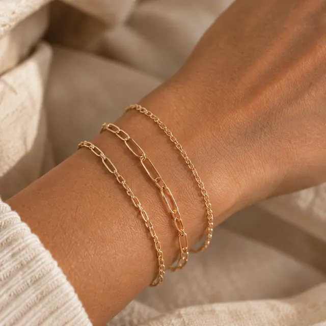 A wrist wearing three fine gold chain bracelets, resting on soft linen